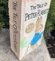Brick painted as cover of "The Tale of Peter Rabbit" featuring a brown rabbit in a blue coat.
