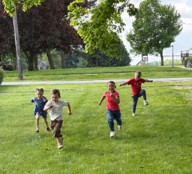 A group of four preschool children race across a green lawn.