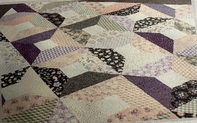 A handmade mosaic quilt in florals and patterns. Colors include purples, greens, pinks, and white.
